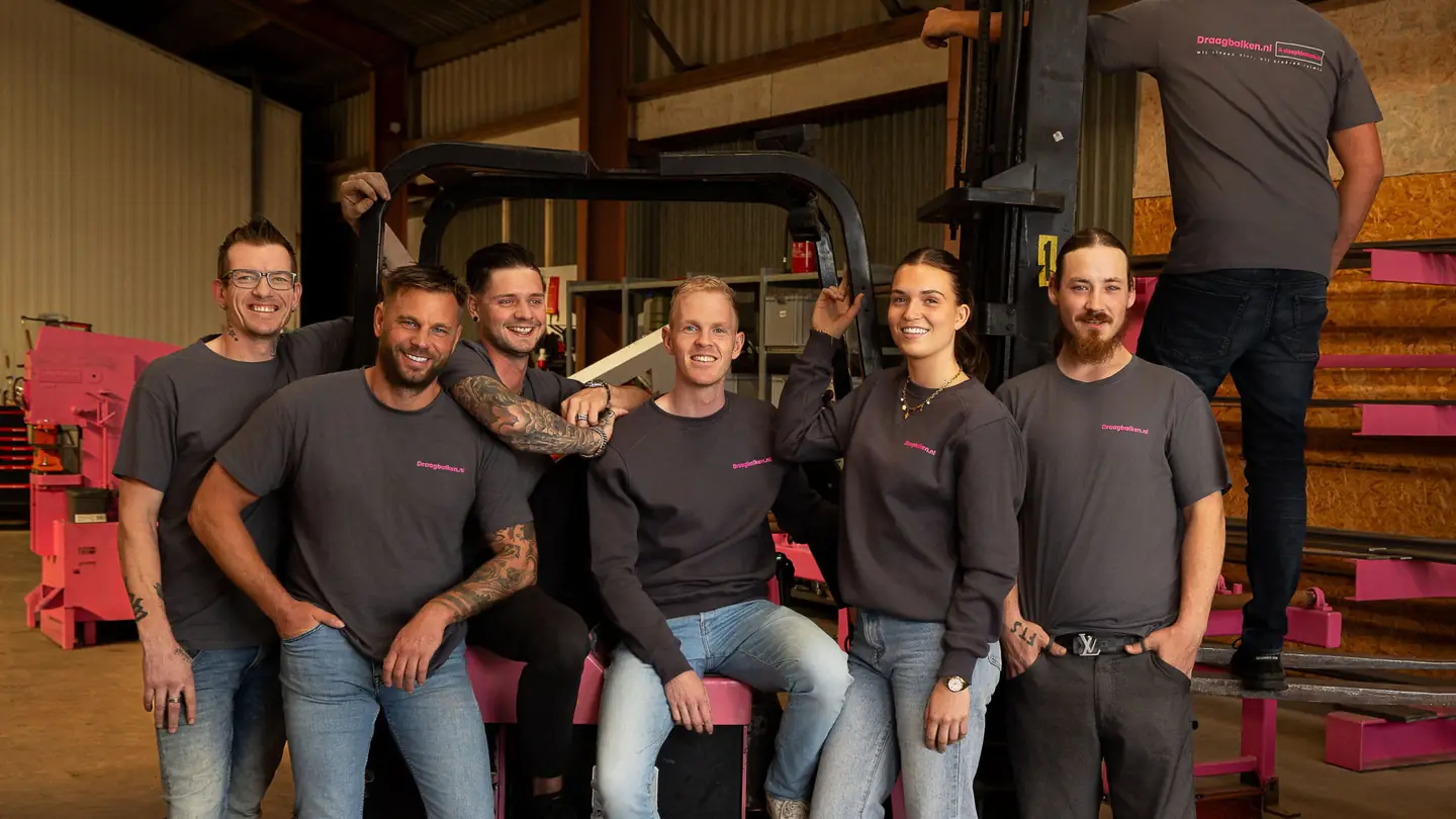 Het voltallige team van Draagbalken.nl rond de roze heftruck in de loods in Nibbixwoud